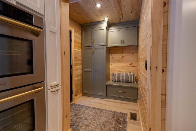 kitchen featuring wood walls, wood ceiling, gray cabinets, double oven, and light hardwood / wood-style floors