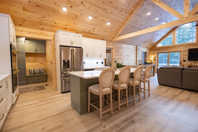 kitchen with high vaulted ceiling, wood walls, an island with sink, stainless steel fridge, and wooden ceiling