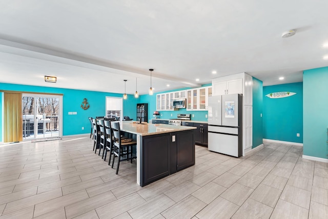 kitchen with a kitchen island, white cabinets, hanging light fixtures, light stone counters, and stainless steel appliances