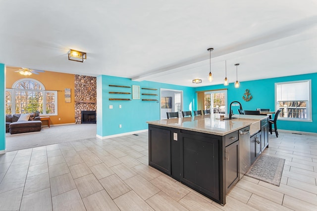 kitchen with sink, decorative light fixtures, an island with sink, a fireplace, and light stone countertops