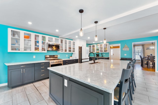 kitchen with appliances with stainless steel finishes, decorative light fixtures, white cabinets, light stone counters, and a spacious island