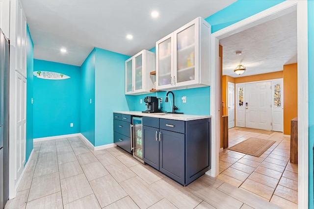 kitchen with white cabinetry, sink, blue cabinetry, and beverage cooler