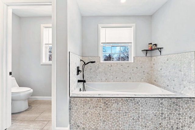 bathroom with toilet, tile patterned flooring, and tiled tub