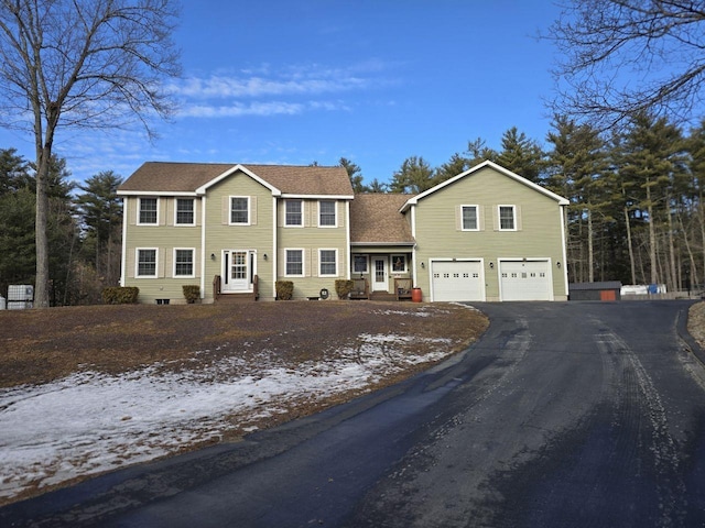 colonial home with driveway, roof with shingles, and an attached garage