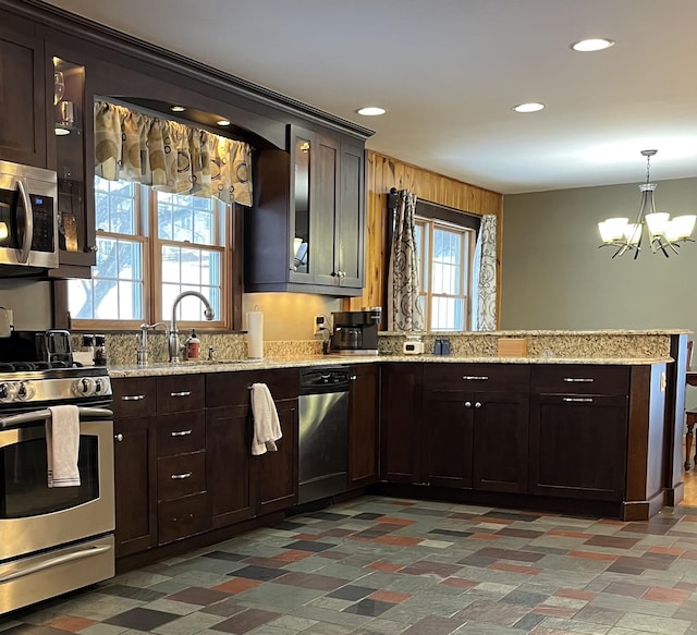 kitchen with pendant lighting, sink, an inviting chandelier, wooden walls, and stainless steel appliances