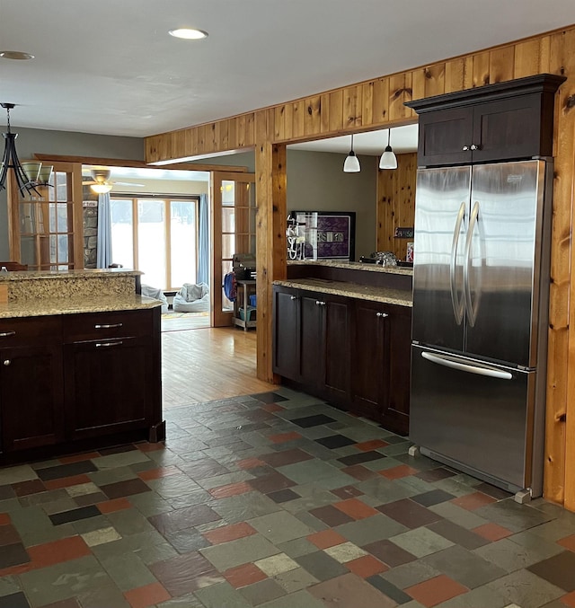 kitchen with wooden walls, stainless steel fridge, and dark brown cabinets