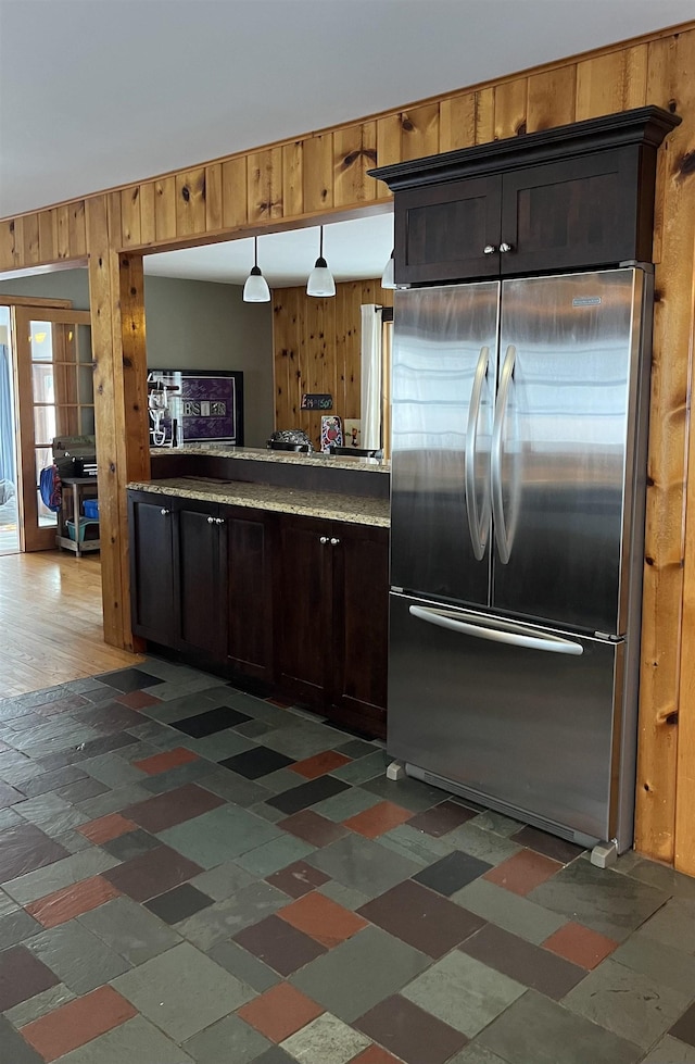 kitchen with hanging light fixtures, stainless steel fridge, and wood walls