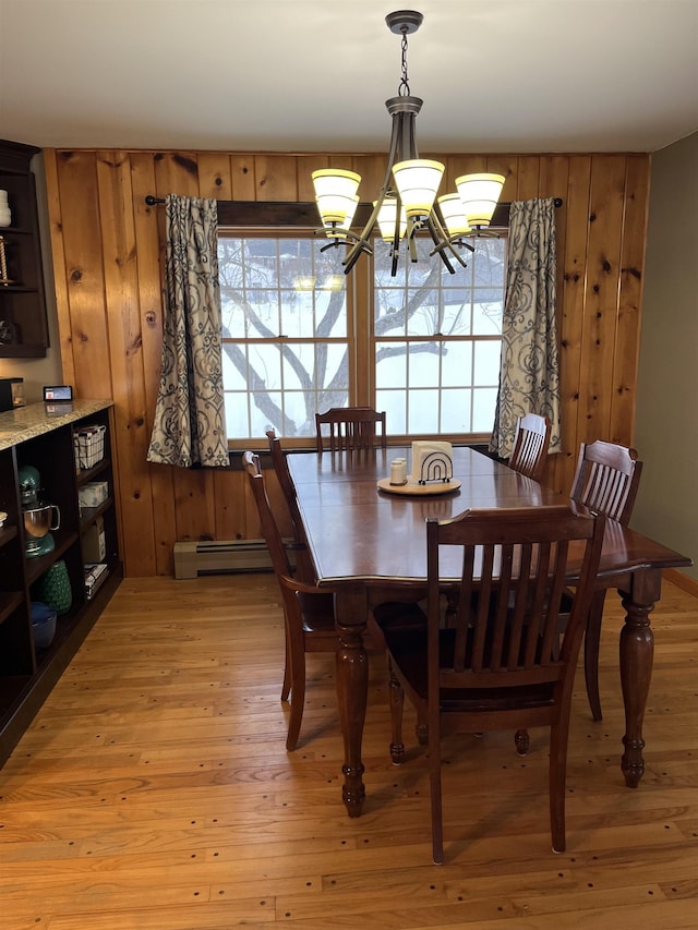 dining area featuring an inviting chandelier, a baseboard radiator, wooden walls, and light hardwood / wood-style floors