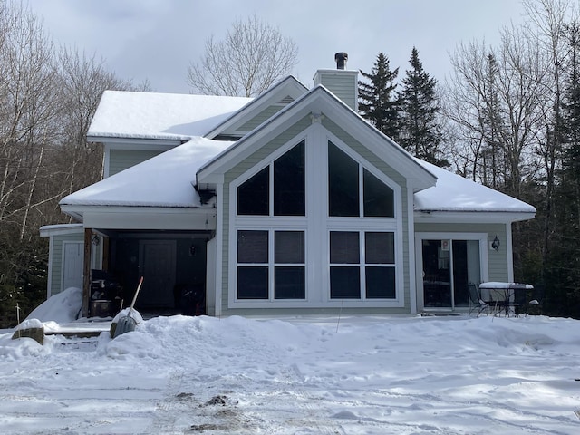 snow covered rear of property featuring a chimney