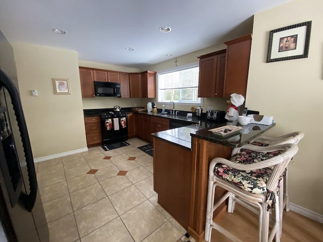 kitchen with a kitchen bar, black appliances, kitchen peninsula, and light tile patterned flooring