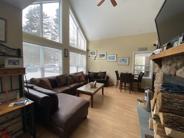 living room featuring a towering ceiling, a fireplace, ceiling fan, and light wood-type flooring