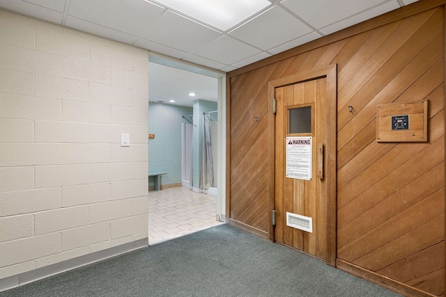 corridor featuring wooden walls, dark carpet, and a drop ceiling