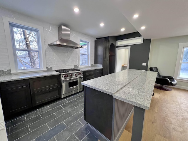 kitchen featuring high end stainless steel range oven, backsplash, light stone counters, ventilation hood, and a kitchen island