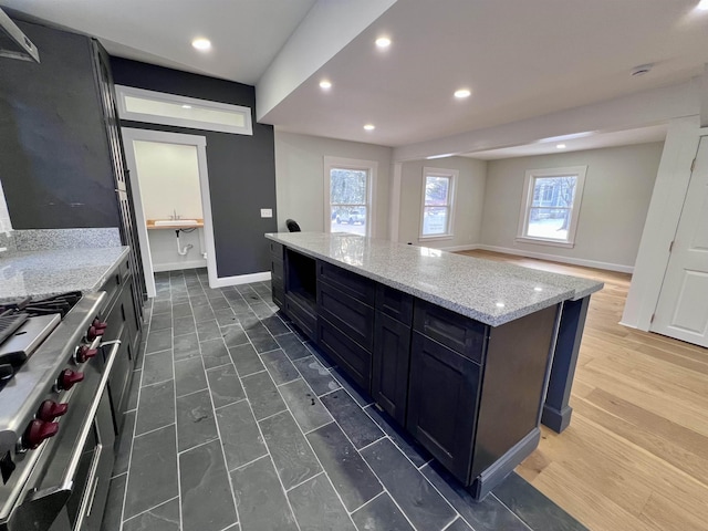 kitchen featuring light stone counters, sink, high end stove, and a center island