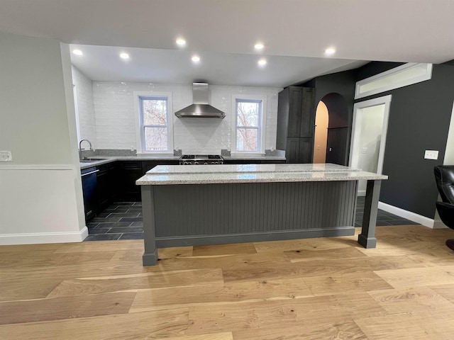 kitchen with wall chimney range hood, light stone countertops, and a kitchen island