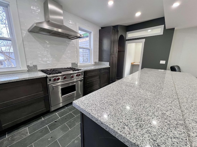 kitchen featuring island exhaust hood, light stone countertops, backsplash, and designer range