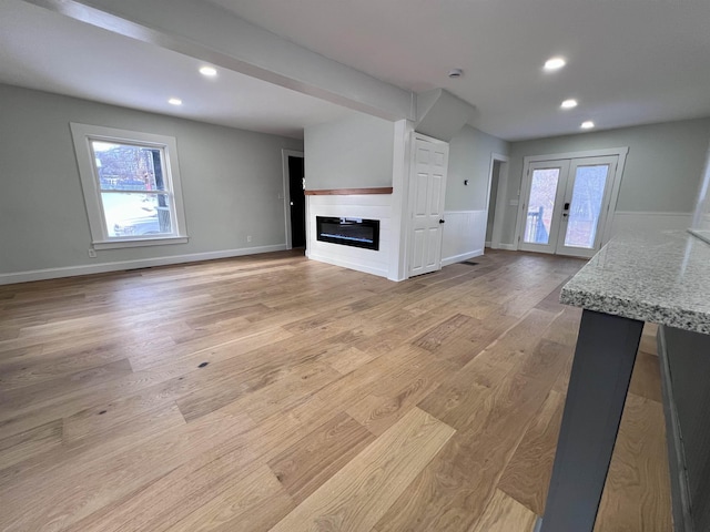 unfurnished living room featuring french doors, a healthy amount of sunlight, and light wood-type flooring