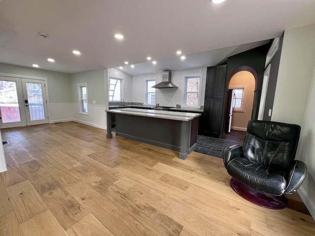 kitchen featuring wall chimney exhaust hood, a breakfast bar area, plenty of natural light, a kitchen island, and light hardwood / wood-style floors