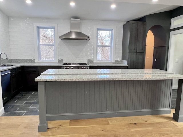 kitchen featuring range, light stone countertops, wall chimney exhaust hood, and a kitchen island