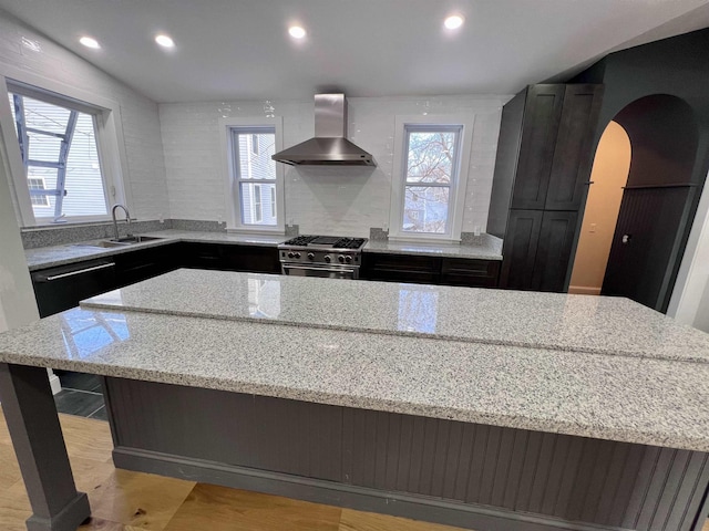 kitchen featuring sink, high end range, light stone counters, a kitchen island, and wall chimney exhaust hood