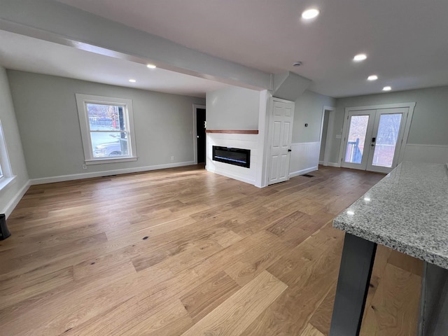 unfurnished living room featuring plenty of natural light, light hardwood / wood-style floors, and french doors