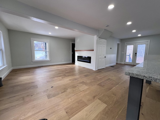 unfurnished living room featuring french doors, light hardwood / wood-style flooring, and a wealth of natural light