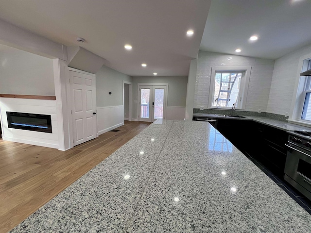 kitchen featuring french doors, sink, light stone counters, oven, and hardwood / wood-style floors