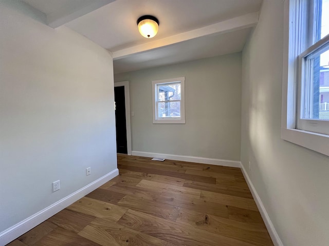 spare room with beam ceiling and light hardwood / wood-style flooring