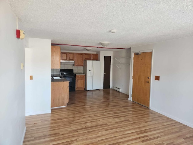 kitchen with under cabinet range hood, black range with electric stovetop, white refrigerator with ice dispenser, brown cabinets, and dark countertops