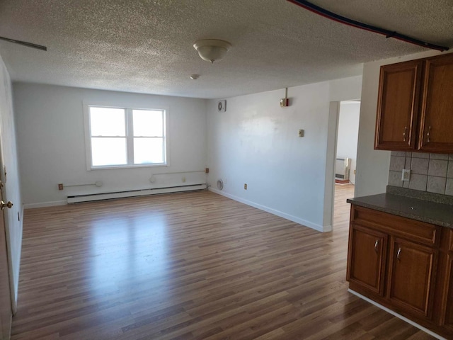 interior space with a baseboard heating unit, a textured ceiling, baseboards, and wood finished floors