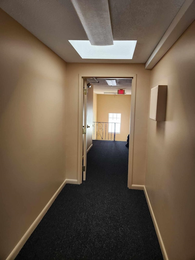 hallway with carpet floors, a skylight, a textured ceiling, and baseboards