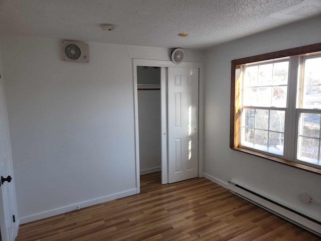 unfurnished bedroom with a textured ceiling, a baseboard radiator, wood finished floors, and baseboards