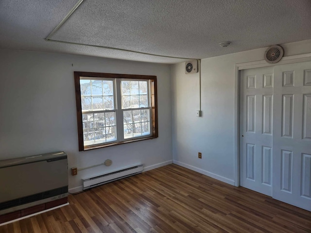 spare room with baseboards, visible vents, dark wood-style flooring, a textured ceiling, and a baseboard heating unit