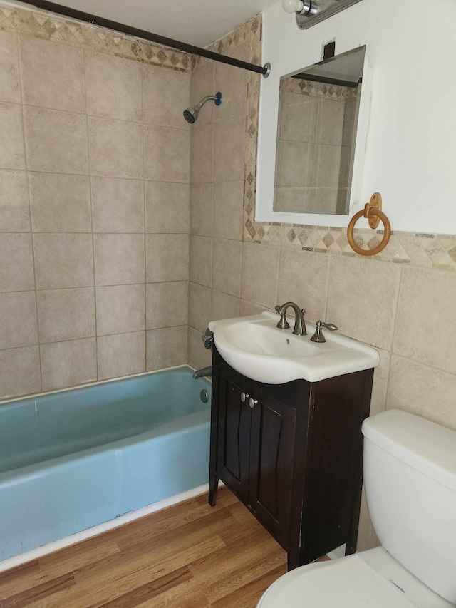 bathroom featuring shower / bathtub combination, toilet, wood finished floors, vanity, and tile walls