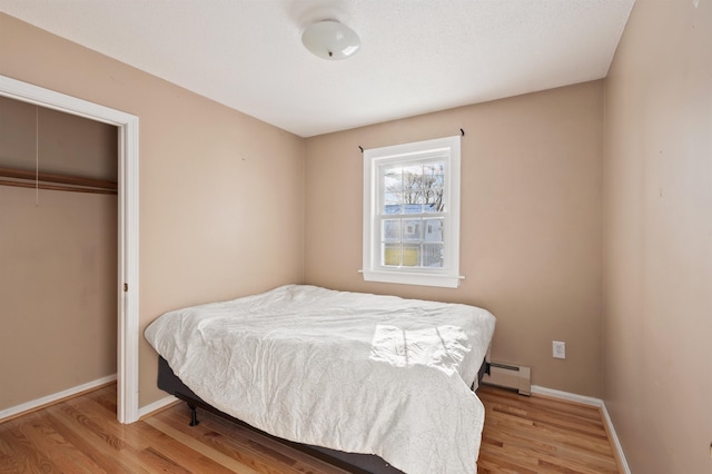 bedroom featuring light wood-type flooring, baseboard heating, and a closet