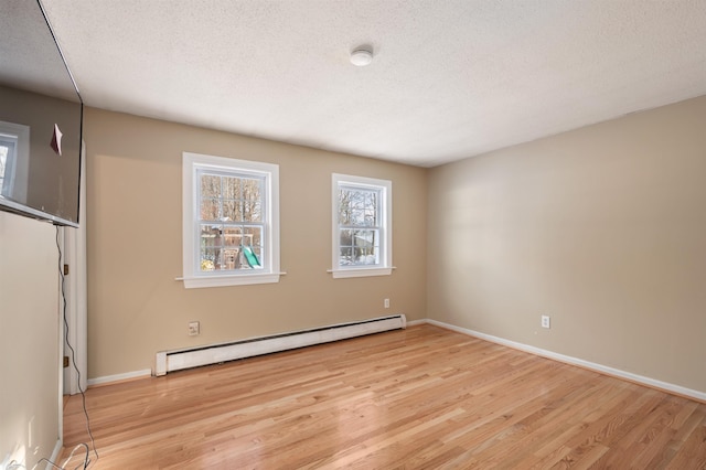 spare room with a textured ceiling, baseboard heating, and light hardwood / wood-style floors