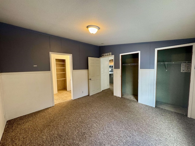 unfurnished bedroom featuring a textured ceiling, vaulted ceiling, light carpet, and two closets