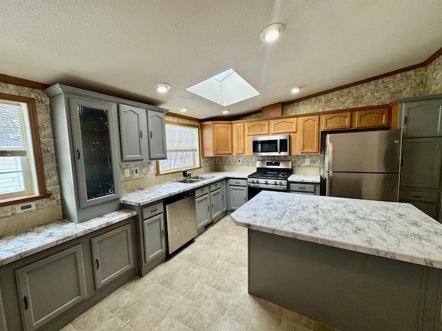 kitchen featuring lofted ceiling with skylight, sink, crown molding, appliances with stainless steel finishes, and gray cabinets