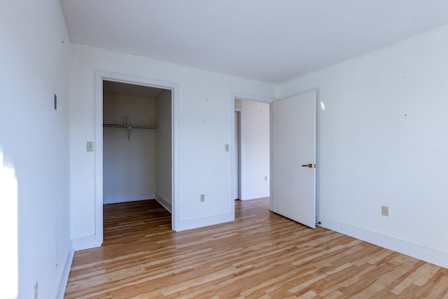 unfurnished bedroom with a spacious closet, a closet, and light wood-type flooring