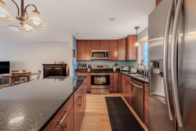 kitchen featuring sink, light hardwood / wood-style flooring, appliances with stainless steel finishes, dark stone countertops, and decorative light fixtures