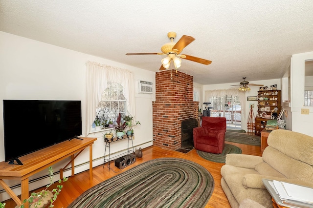 living room featuring a wall mounted air conditioner, wood-type flooring, ceiling fan, a brick fireplace, and a textured ceiling