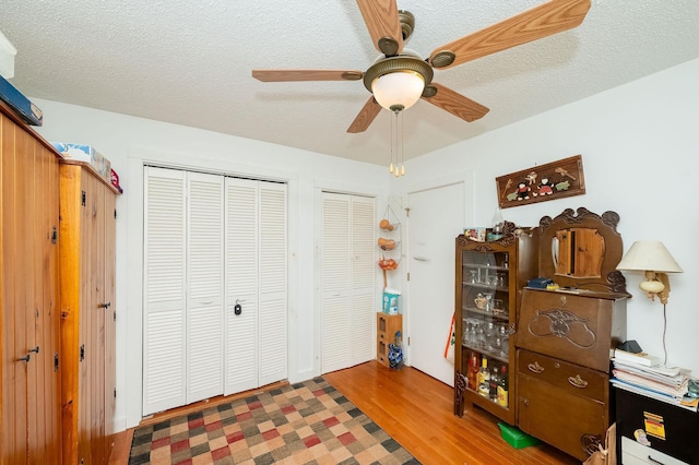 bedroom featuring multiple closets, a textured ceiling, wood-type flooring, and ceiling fan