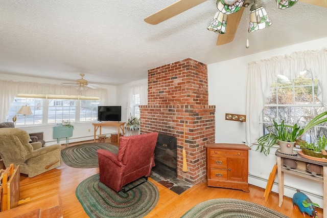 living room featuring a textured ceiling, baseboard heating, ceiling fan, a fireplace, and light hardwood / wood-style floors