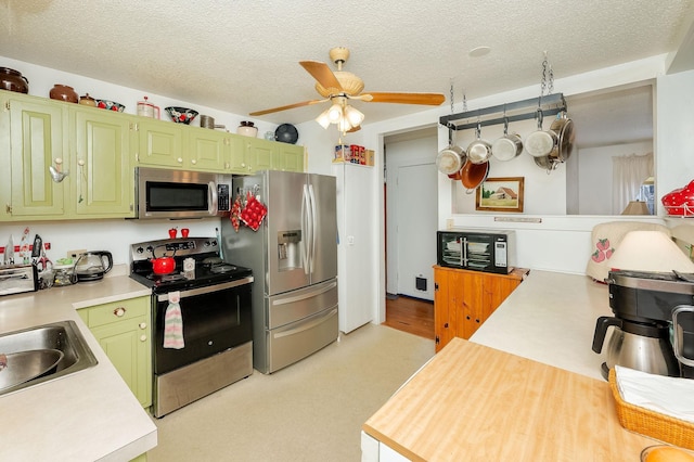 kitchen with green cabinetry, stainless steel appliances, sink, and a textured ceiling