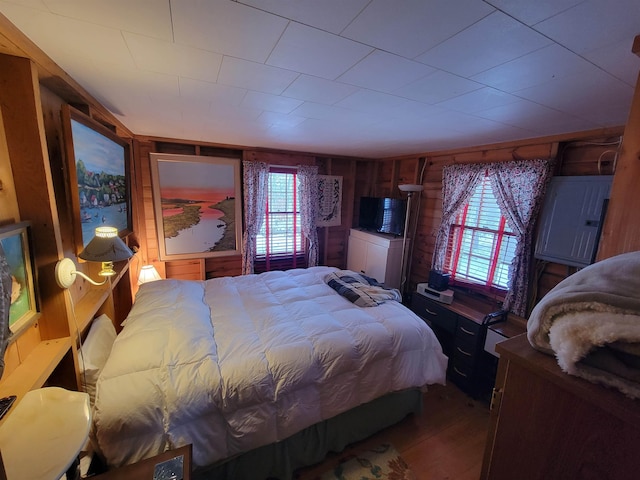 bedroom with hardwood / wood-style flooring, wooden walls, and electric panel