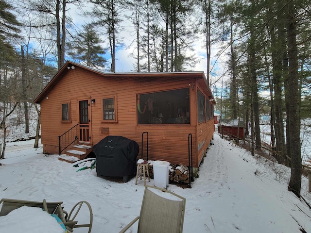 snow covered rear of property with a sunroom