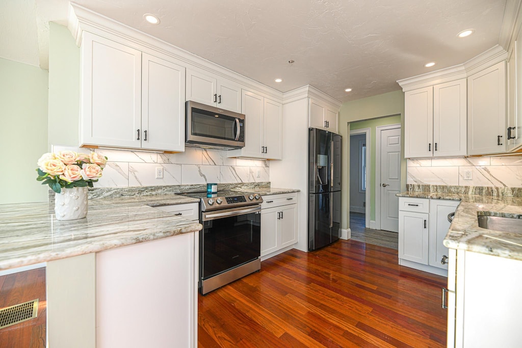 kitchen with dark wood-type flooring, kitchen peninsula, stainless steel appliances, decorative backsplash, and white cabinets