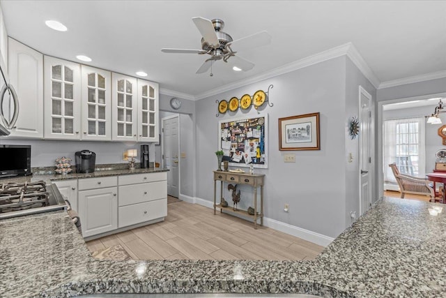 kitchen with white cabinetry, crown molding, light hardwood / wood-style floors, and dark stone countertops