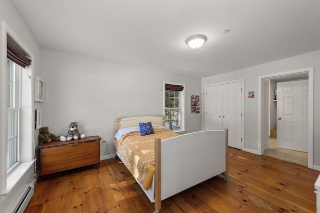 bedroom with baseboard heating, hardwood / wood-style floors, and a closet