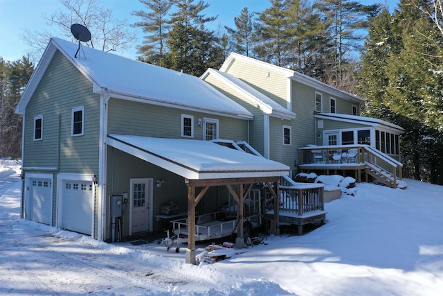 snow covered rear of property with a garage, a wooden deck, and a sunroom